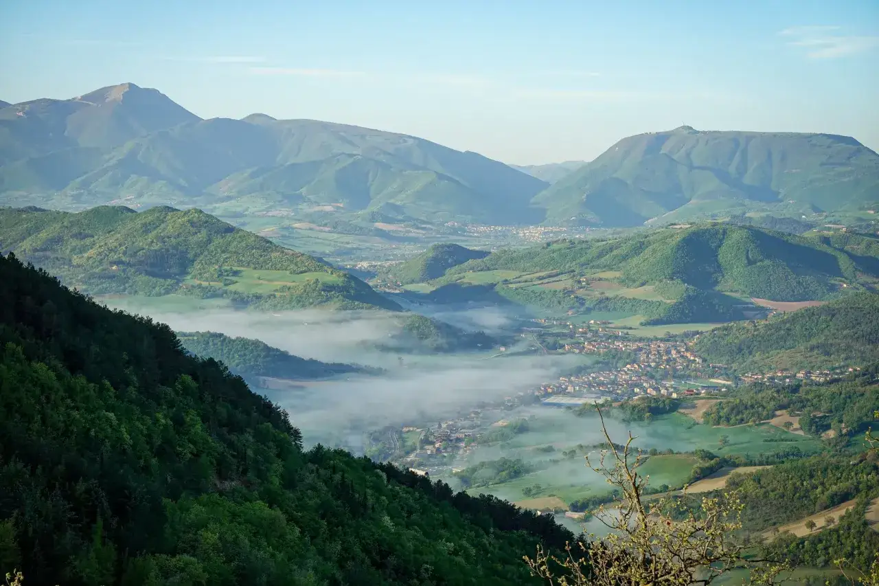 Panoramica mozzafiato su Acqualagna, con nebbia che avvolge la valle e montagne verdi. Un luogo incantevole da scoprire.