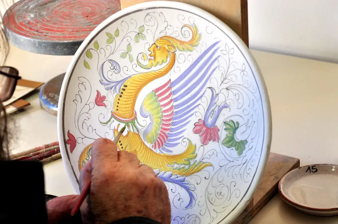 Un artista dipinge un grifone su un piatto di ceramica a Deruta, Perugia. I colori vivaci prendono vita sotto il pennello.