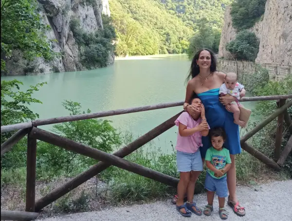 Famiglia felice nella golena del Furlo, con un lago turchese e montagne verdi sullo sfondo.