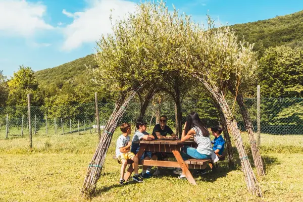 Bambini riuniti attorno a un tavolo da picnic sotto una tettoia naturale nel bosco dei folletti Urbania.
